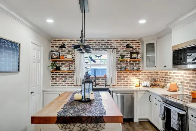 Humble Residence kitchen in Midland with a red brick backsplash, butcher-block island, open shelves and white cabinets