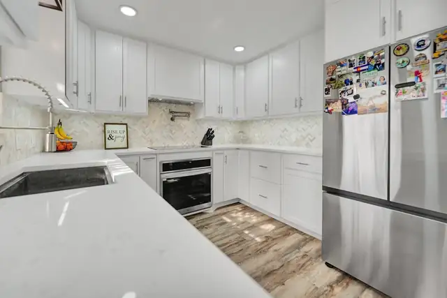 Ward Residence kitchen in Midland with white shaker cabinets, quartz counters, a pull-down faucet and stainless refrigerator