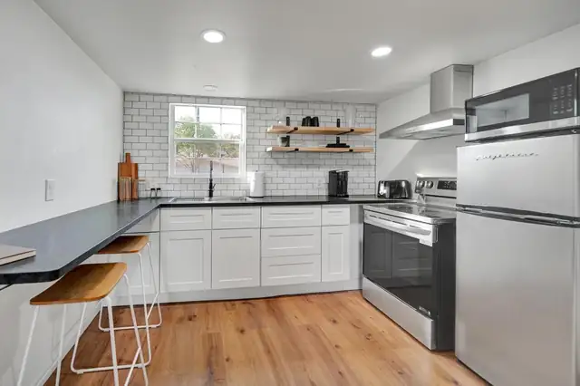 Michigan Residence kitchen in Midland with white shaker cabinets, a black counter with a breakfast bar, subway tile and floating wood shelves
