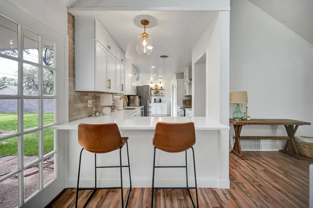 Camarie Residence remodel in Midland with a white kitchen peninsula, leather counter stools and wood-look floors
