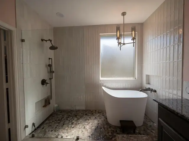 Midland wet room with a freestanding tub inside a glass-enclosed shower, pebble tile floor, white stacked tile and bronze fixtures